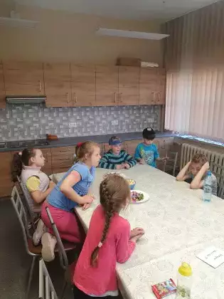 Dzieci przy wspólnym stole częstują się słodyczami.