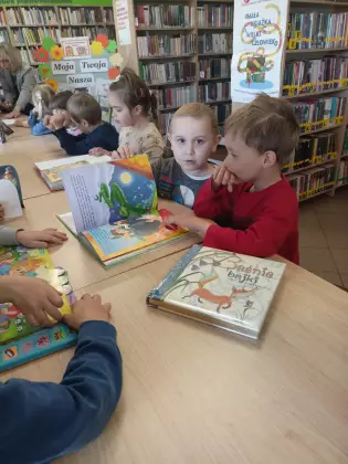 Dzieci siedzą przy stole i oglądają książki.