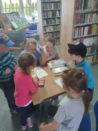 Dzieci stoją przy stoliku i rozwiązują krzyżówkę.