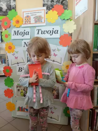 Dziewczynki pozują do zdjęcia pod gazetką biblioteczną.