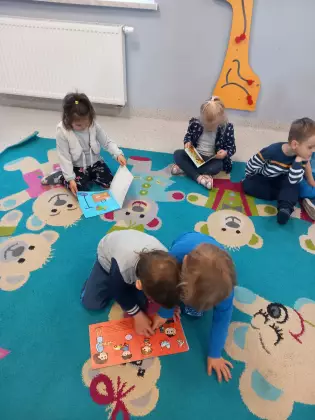 Przedszkolaki siedzą na dywanie i oglądają książki przyniesione z biblioteki.