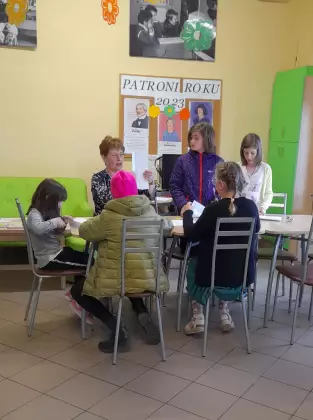 Dziewczyny razem z bibliotekarką siedzą przy stole i oglądają książki.