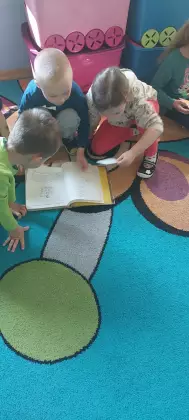 Przedszkolak siedzą na dywanie i ogląda książkę.