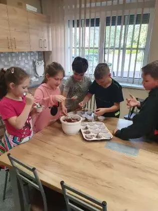 Dzieci wkładają surowe ciasto do papilotek na muffinki.