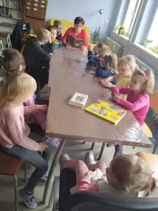 Dzieci siedzą przy stole i słuchają bajki czytanej przez panią.
