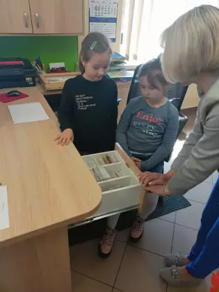 Dziewczynki stoją przy biurku i poznają pracę bibliotekarza.