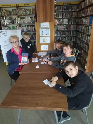 Dzieci z Panią bibliotekarką siedzą przy stole i pozują do wspólnego zdjęcia.
