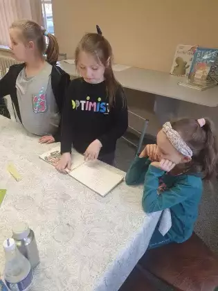 Dziewczyny na zajęciach w bibliotece sklejają zniszczoną książkę.