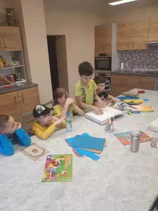 Uczestnicy zajęć siedzą przy stole i słuchają czytanej książki.