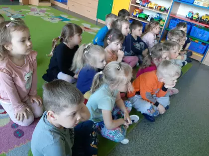 Maluszki siedzą na dywanie w przedszkolu i słuchają czytanej książki.