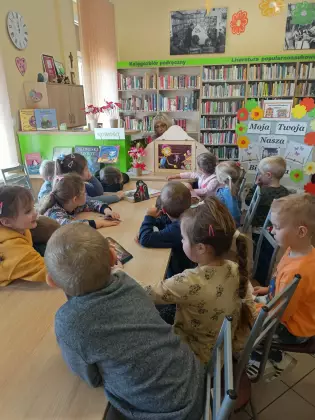 Przedszkolaki siedzą przy stole i słuchają opowiadania czytanego za pomocą teatrzyku kamishibai.