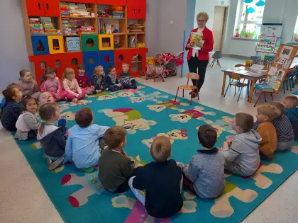 Dzieci siedzą na dywanie i słuchają bibliotekarki