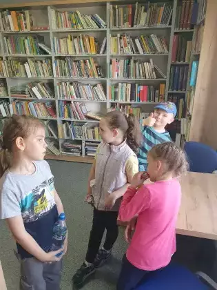 Dzieci stoją w bibliotece i grają w podchody.