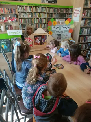 Dzieci słuchają opowiadania czytanego za pomocą teatrzyku Kamishibai.