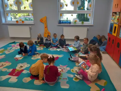 Przedszkolaki siedzą na dywanie i oglądają książeczki.