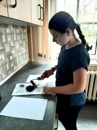 Uczestniczka zajęć maluje obraz czarną farbą.