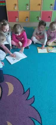 Przedszkolaki na dywanie oglądają książki.