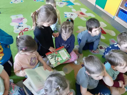 Maluszki siedzą na dywanie i oglądają książeczki przyniesione z biblioteki.