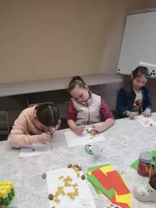 Dziewczynki  siedzą przy stole i wykonują pracę plastyczną.