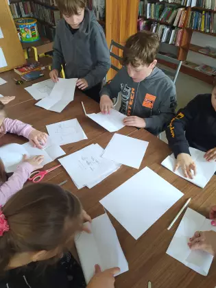 Uczestnicy zajęć składają mini książeczki z papieru.