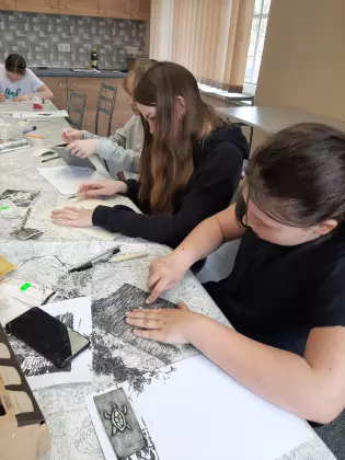 Nastolatki siedzą przy stole i rysują pracę plastyczną.