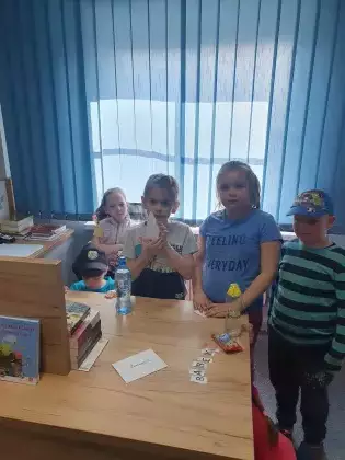 Uczestnicy zajęć stoją przy biurku bibliotekarza.