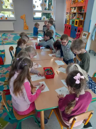 Dzieci siedzą przy stolikach i wykonują pracę plastyczną.