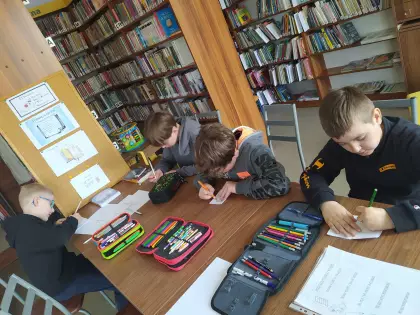 Chłopcy na zajęciach w bibliotece tworzą pracę plastyczną.