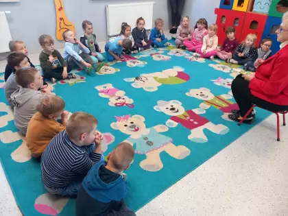 Przedszkolaki siedzą na dywanie i słuchają czytanej bajki.
