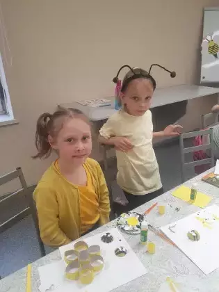 Dziewczynki na zajęciach w bibliotece sklejają plaster miodu z rolek papierowych.