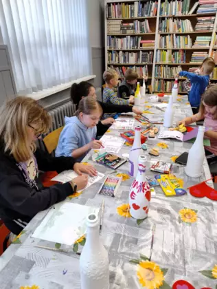 Dzieci siedzą przy stole i malują farbkami prezent dla mamy..