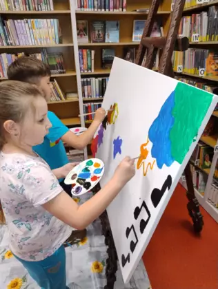 Dzieci na dużej kartce malują farbami obraz.