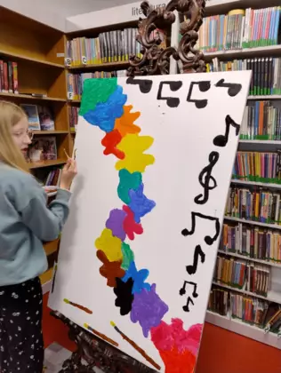 Dzieci na dużej kartce malują farbami obraz.