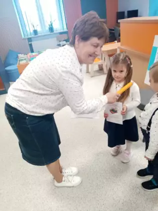 Pani bibliotekarka pasuje młodsze dzieci na czytelników.