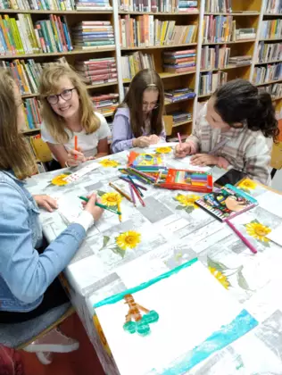 Dziewczyny siedzą przy stole i malują mazakami obrazki.