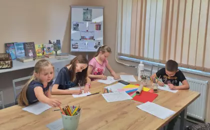 Dzieci siedzą przy stole i malują mola książkowego.