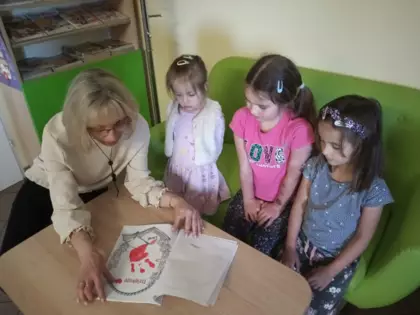 Dzieci wraz z bibliotekarką oglądają książeczkę.