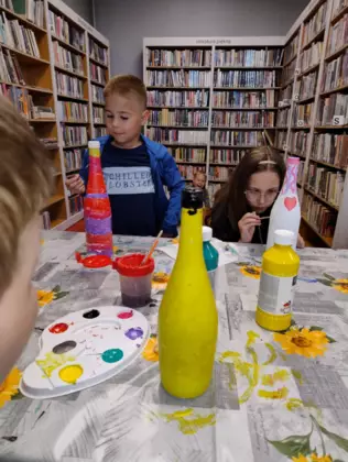 Dzieci siedzą przy stole i malują farbkami prezent dla mamy