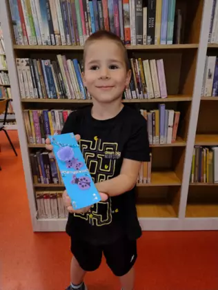 Chłopczyk trzyma w rękach zakładkę do książki wykonaną na zajęciach.