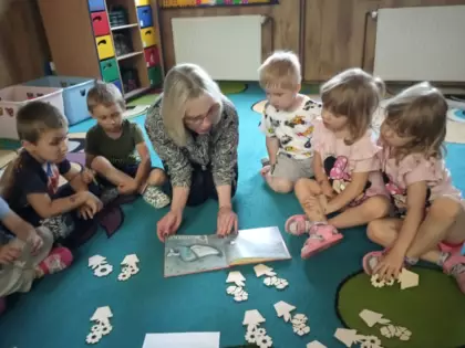 Przedszkolaki siedzą na dywanie i słuchają czytanej książeczki.