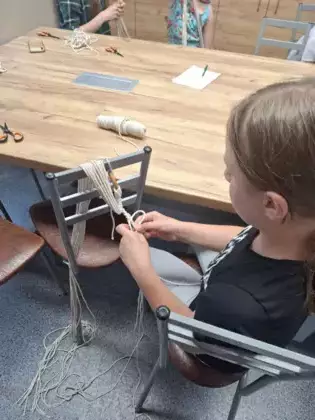 Uczestniczka plecie ze sznurka kwietnik dla mamy.