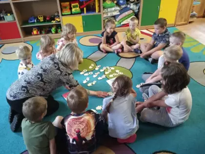 Przedszkolaki na dywanie oglądają kwiatuszki dla mamy.