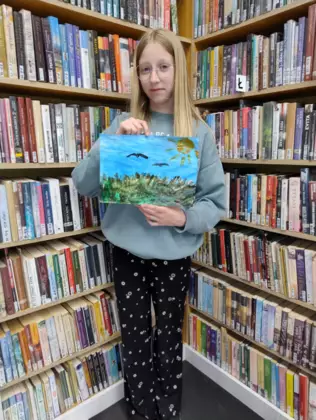 Dziewczynka pozuje do zdjęcia ze swoim obrazem namalowanym farbami.