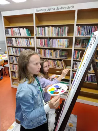 Dzieci na dużej kartce malują farbami obraz.