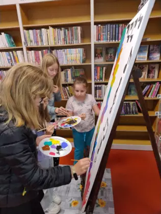 Dzieci na dużej kartce malują farbami obraz.