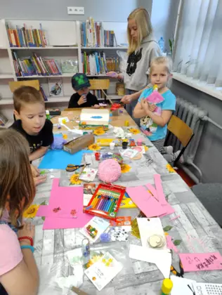 Dzieci siedzą przy stoliku i wykonują zakładki do książki z kolorowego papieru.