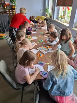 Dzieci siedzą przy stoliku i wykonują prace plastyczne.