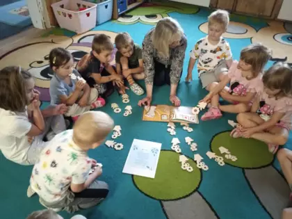 Przedszkolaki siedzą na dywanie i słuchają czytanej książeczki.