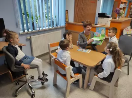 Przedszkolaki słuchają książeczki czytanej przez panią bibliotekarkę.