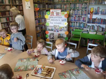 Przedszkolaki siedzą przy stole na poczęstunku.